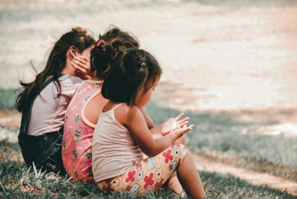 Three children sitting in a sunny meadow.